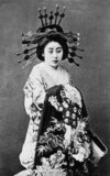 Oiran (花魁) were the courtesans of Edo period Japan. The oiran were considered a type of yūjo (遊女) 'woman of pleasure' or prostitute. However, they were distinguished from the yūjo in that they were entertainers, and many became celebrities of their times outside the pleasure districts. Their art and fashions often set trends among the wealthy and, because of this, cultural aspects of oiran traditions continue to be preserved to this day.<br/><br/>

The oiran arose in the Edo period (1600–1868). At this time, laws were passed restricting brothels to walled districts set some distance from the city center. In the major cities these were the Shimabara in Kyoto, the Shinmachi in Osaka, and the Yoshiwara in Edo (present-day Tokyo).<br/><br/>

These rapidly grew into large, self-contained 'pleasure quarters' offering all manner of entertainments. Within, a courtesan’s birth rank held no distinction, which was fortunate considering many of the courtesans originated as the daughters of impoverished families who were sold into this lifestyle as indentured servants. Instead, they were categorized based on their beauty, character, education, and artistic ability.<br/><br/>

Among the oiran, the tayū (太夫) was considered the highest rank of courtesan and were considered suitable for the daimyo or feudal lords. In the mid-1700s courtesan rankings began to disappear and courtesans of all classes were collectively known simply as 'oiran'.<br/><br/>

The word oiran comes from the Japanese phrase oira no tokoro no nēsan (おいらの所の姉さ) which translates as 'my elder sister'. When written in Japanese, it consists of two kanji, 花 meaning 'flower', and 魁 meaning 'leader' or 'first', hence 'Leading Flower' or 'First Flower'.